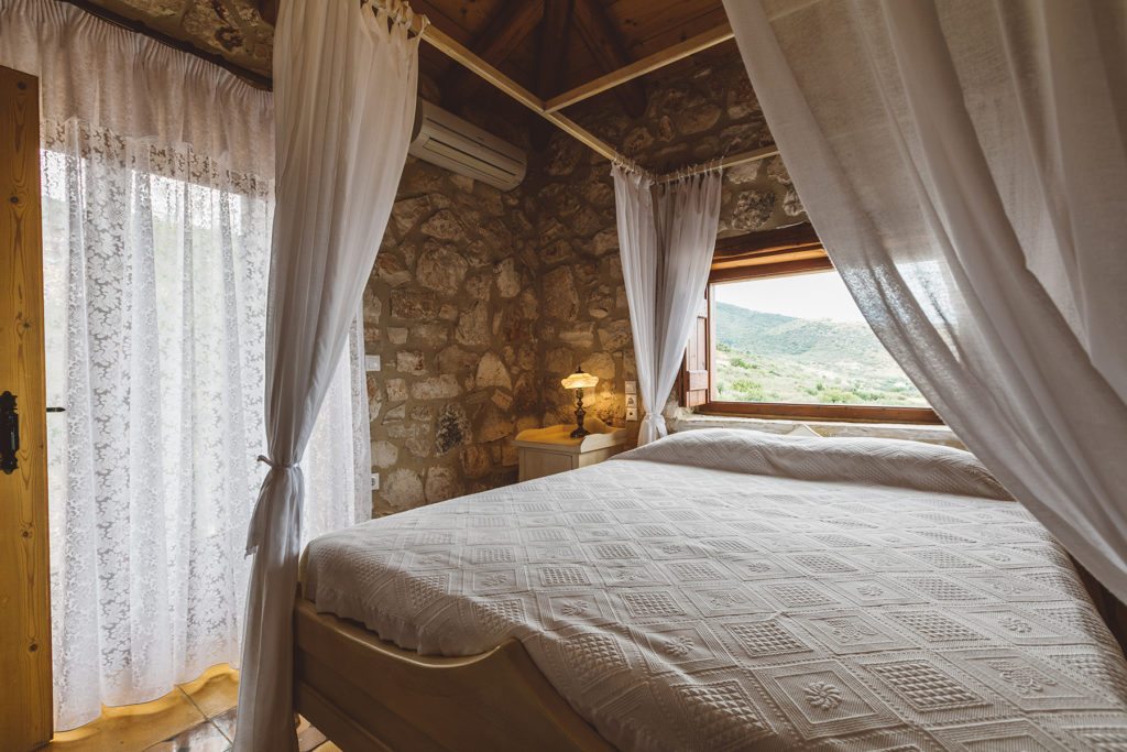 Four poster bed with draped white linens and french windows in the Orfos Villa, Yria