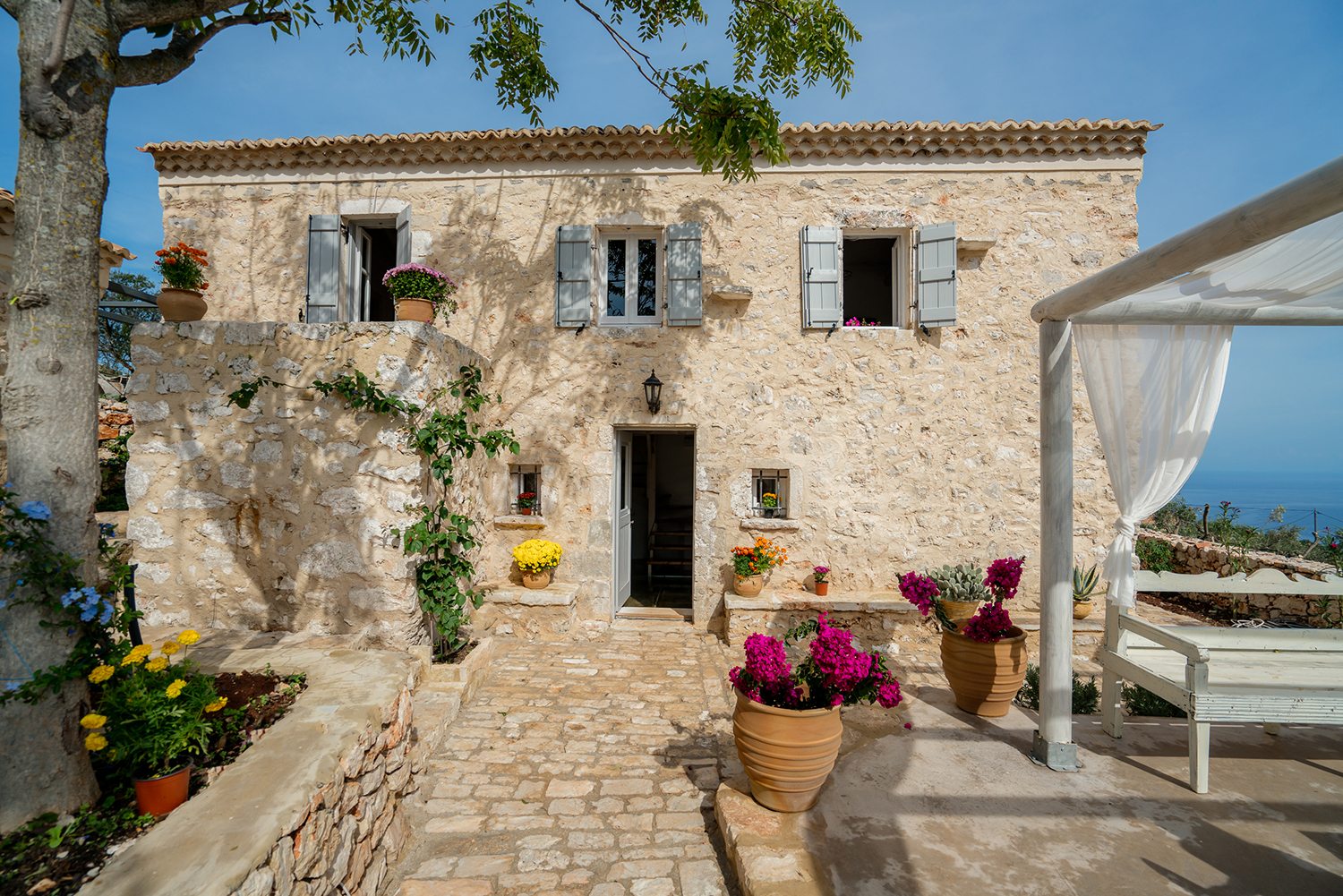 Traditional stone greek villa for 6 people in Zakynthos with blue wooden shutters and plants in terracotta pots