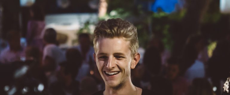 Handsome blonde haired young man smiling at a crowded busy restaurant