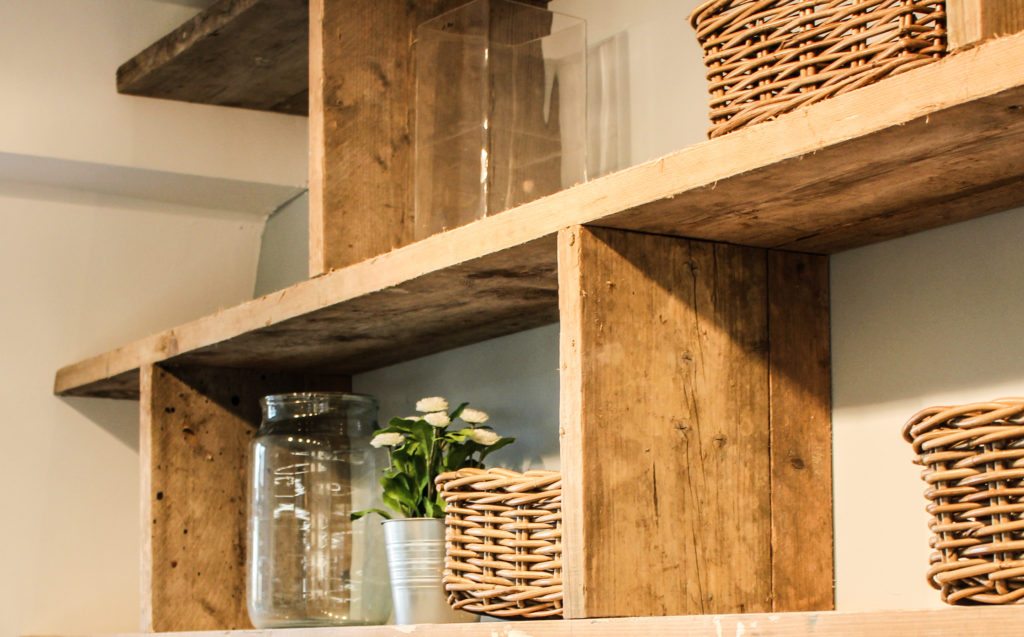 Wooden shelving unit with wicker baskets and glass jars and flower pots
