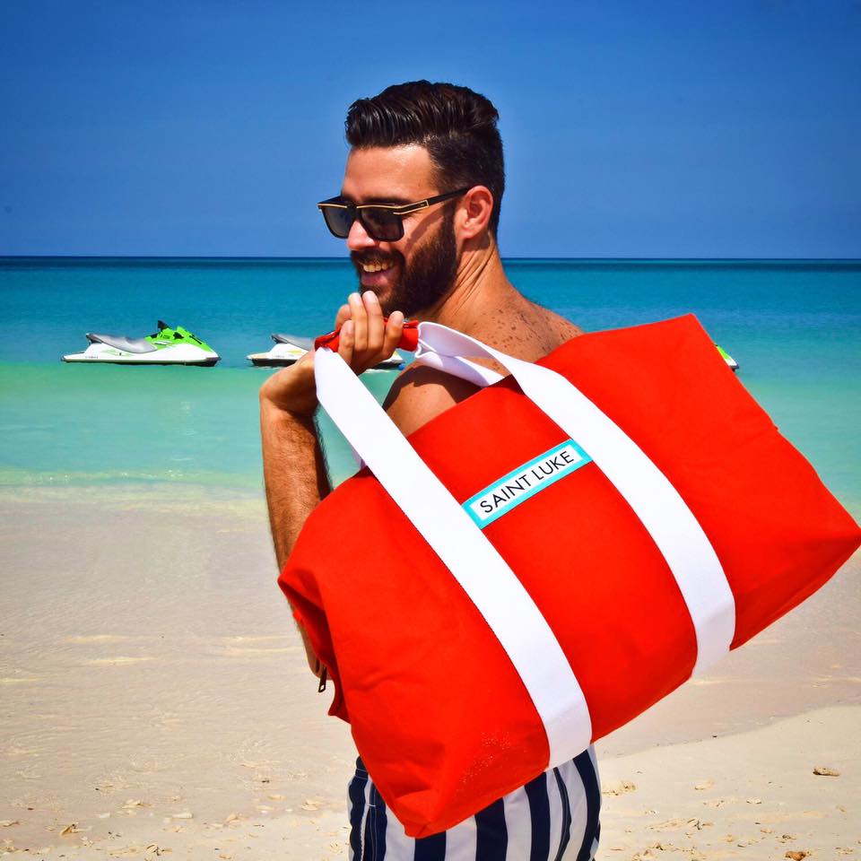 Man in sunglasses carrying a large red holdall