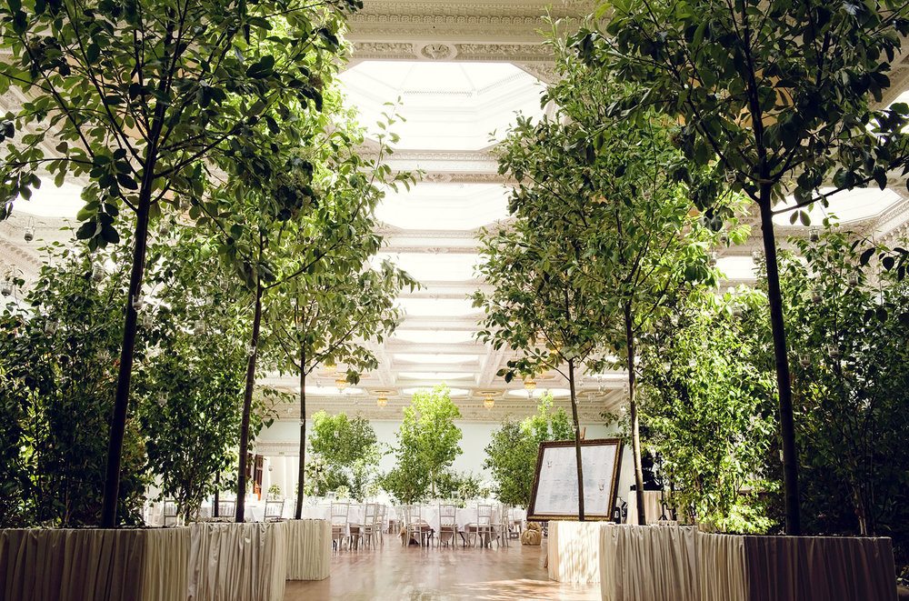 An indoor wedding garden filled with trees and round tables by the Creative Events Agency Riot