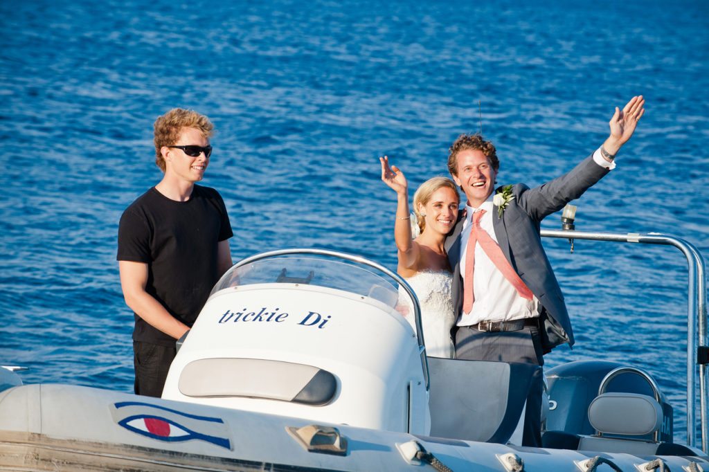 A bride groom getting married in Greece get wave goodbye as they get taken away on a speedboat on the ionian ocean
